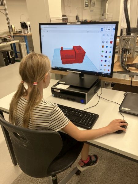 Auf dem Bild ist ein M&auml;dchen am  Computer zu sehen, welches eine  rote Lokomotive in einem 3D- CAD-Programm konstruiert hat.